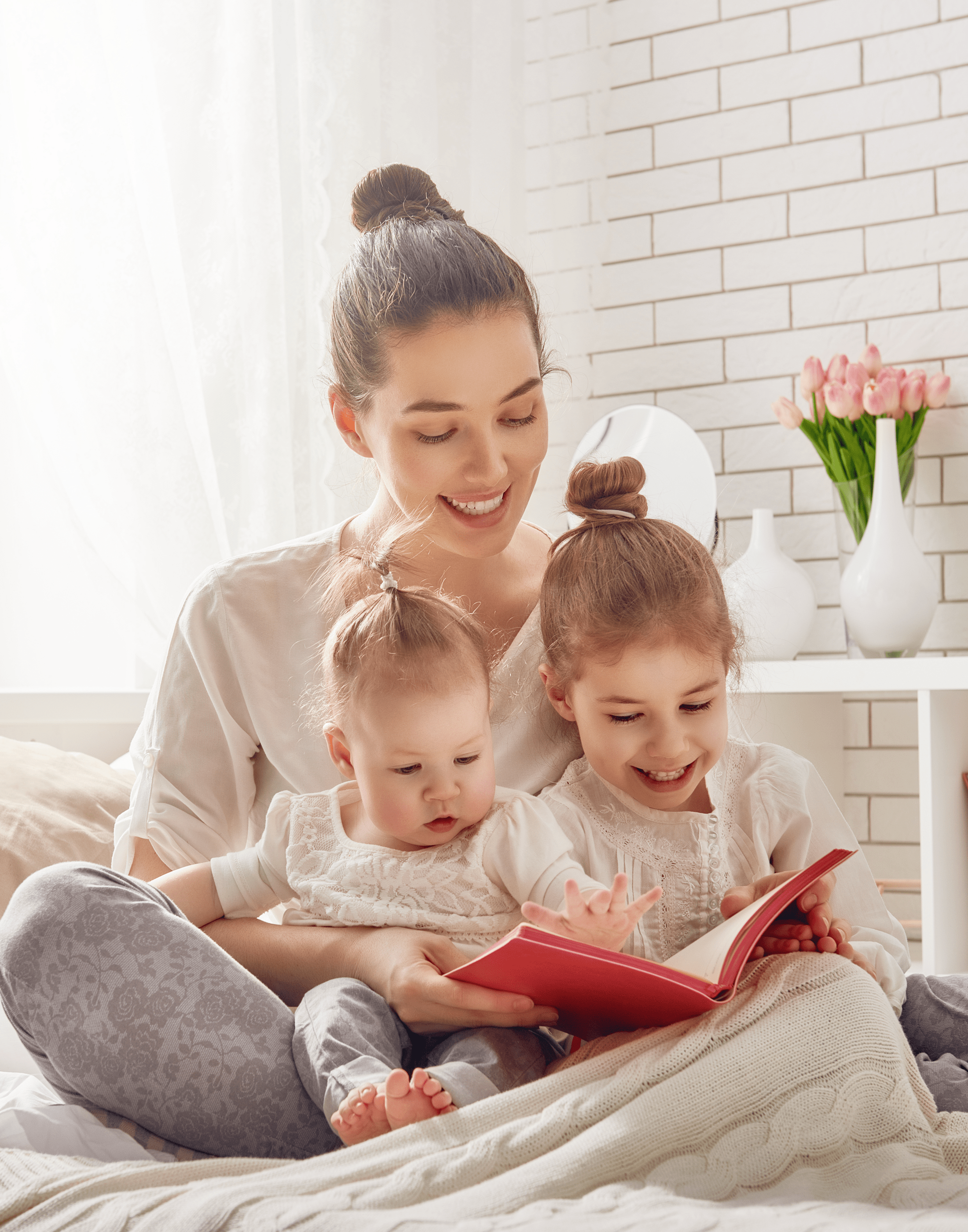 mother reading on the bed with her toddler and infant